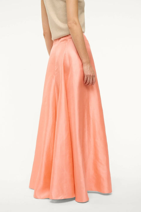 Close up back view of a woman wearing a pink silk, Aline, maxi skirt that features a back zipper and sits at the natural waist, paired with a tan sweater vest. 
