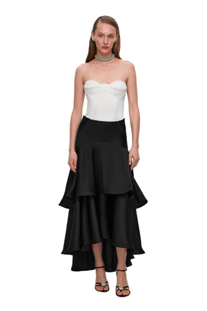 Woman wearing a strapless white top and black ruffled skirt on a white background