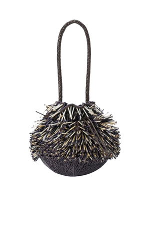 A small round handbag with a dark textured body, covered in dense spiky fringe beads made of black, beige, and white elements, and featuring a single braided shoulder strap, shown on a plain white background.