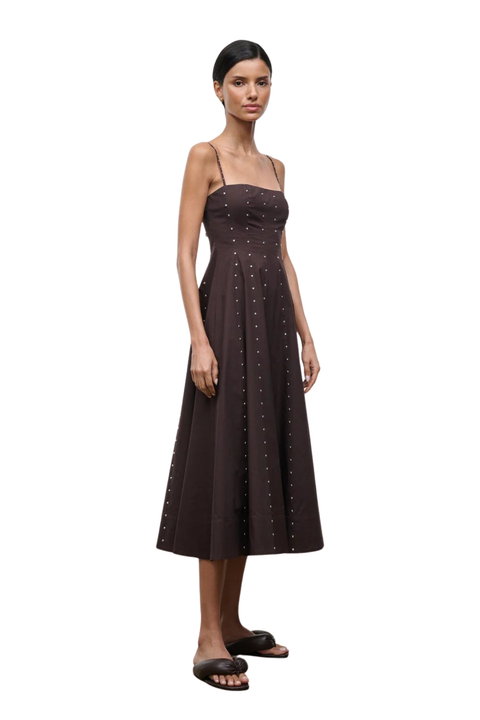 Woman wearing a long brown dress with silver studs on a white background