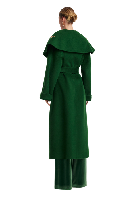 A model shown from the back wearing a dark forest green long coat with a wide collar and matching green wide-leg trousers, set against a plain white background.