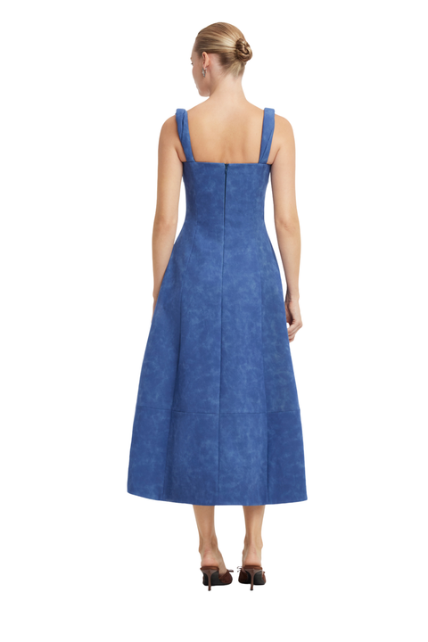 A woman viewed from the back wearing a sleeveless blue midi dress with a structured bodice and flared skirt, paired with dark pointed heels, against a plain white background.