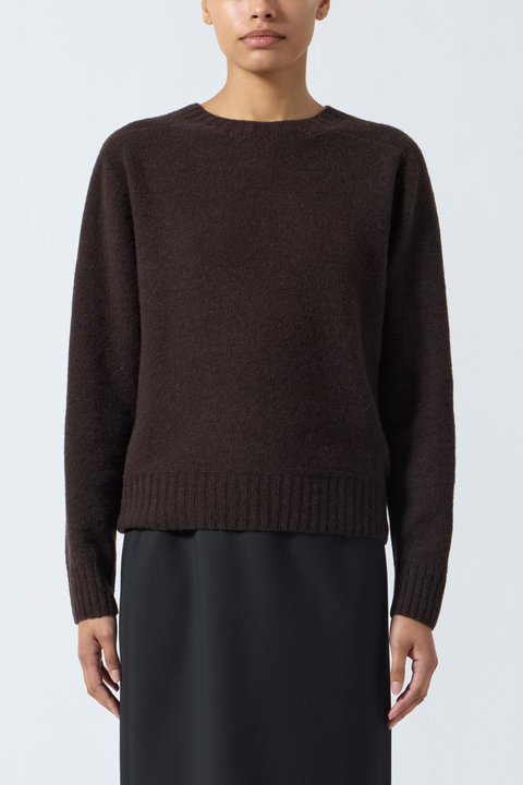 Person wearing a brown crewneck sweater and black skirt on a white background