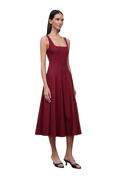 A woman modeling a sleeveless midi dress in deep burgundy with a square neckline and a flared skirt, standing against a plain white background.
