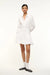 Woman wearing a long sleeve, white mini dress that features a collar and button down detail and a curved yoke at the hem. 