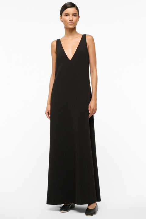 Woman wearing a deep-v black maxi dress paired with black flats. 