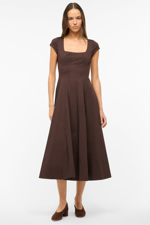 Woman wearing a brown midi dress that features cap sleeves, a square neck, corset styles paneling, and an A-line skirt, paired with brown heels. 