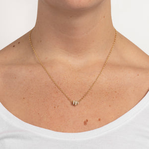 Woman wearing a yellow gold chain necklace that features three yellow gold annulets of differing size, all pave with diamonds. 