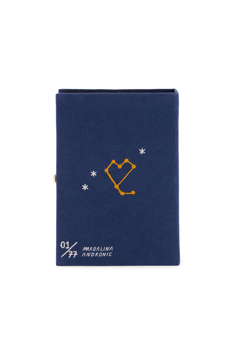 Back of a navy blue book clutch with a gold constellational design and white text reading '01 MICALINA ANDRONIC' on the front, shown against a plain white background.