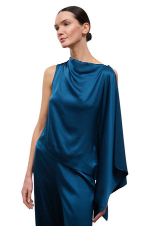 A woman modeling a draped satin one-shoulder top in a deep teal blue color, shown against a plain white background.