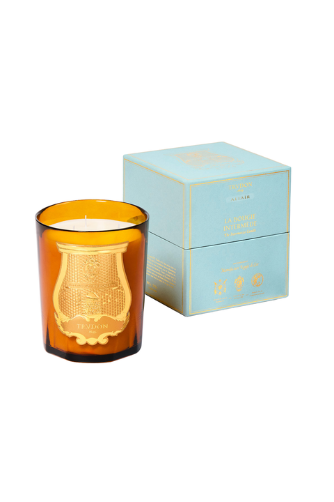 An amber glass jar candle with a gold crest design on the front, shown next to its light blue and gold square packaging box on a white background.