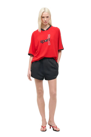 Woman wearing a red sports jersey and black shorts on a white background