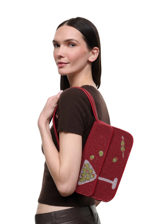A woman wearing a brown t-shirt and dark pants is shown from the side/back, carrying a red textured shoulder bag with a martini graphic on a plain white background.