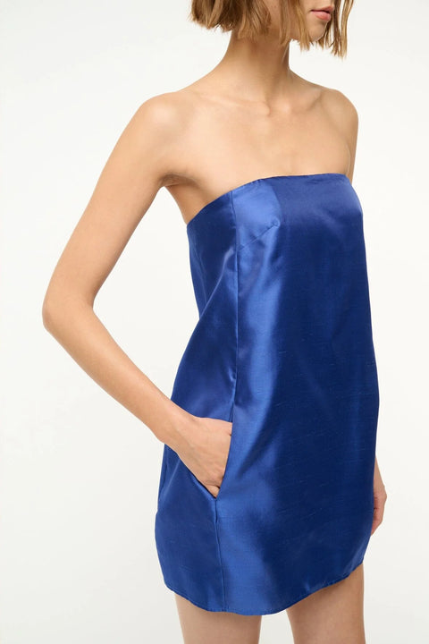 Close up of a woman wearing a royal blue, strapless, silk mini dress that features a soft cocoon silhouette, and hidden pockets.
