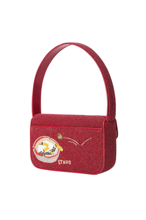 A red textured shoulder bag with a curved top handle, featuring a circular cartoon patch and the brand name 'STAUD' embroidered on the back, set against a plain white background.