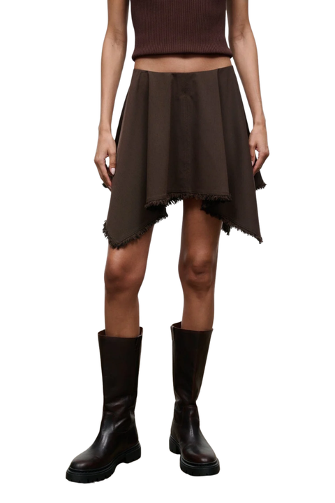 A model wearing a dark brown high-low skirt with a raw, frayed hem, paired with a matching brown ribbed top and dark brown knee-high boots, shown against a plain white background.