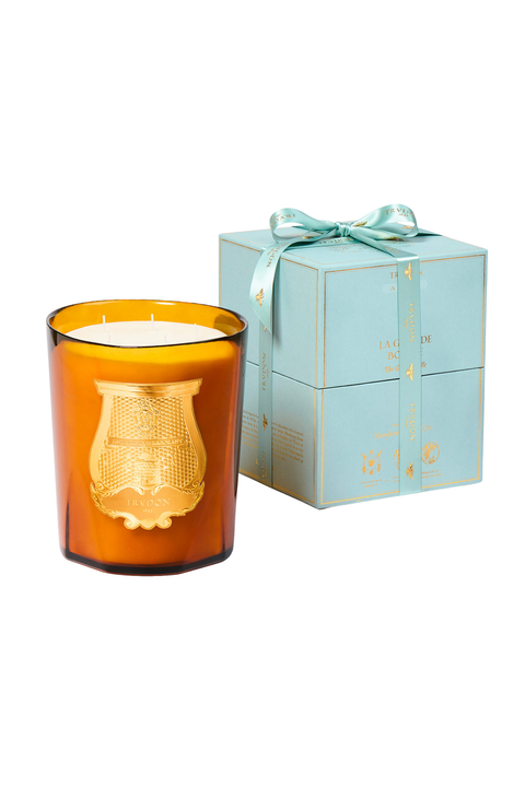 An amber murano glass jar candle with a gold crest emblem on the front, shown next to its light blue gift box tied with a matching ribbon, on a solid white background.