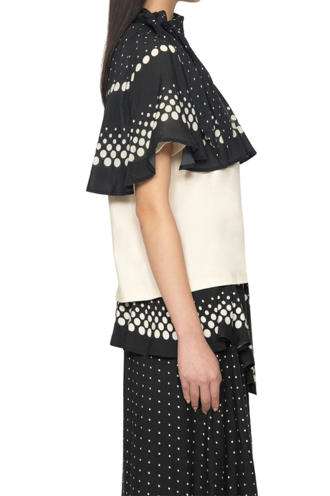 A model shown from the side wearing a black and cream color-blocked top with a polka dot pattern and a matching black skirt with white polka dots, against a plain white background.