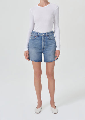 Model facing the camera in the blue denim shorts with a white long sleeve tee
