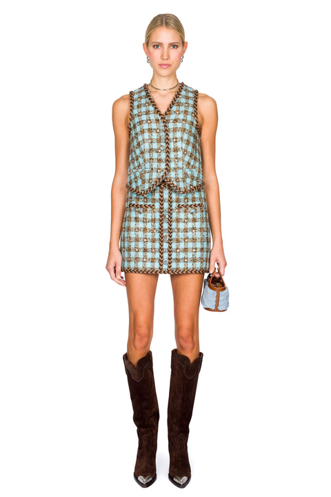 Woman wearing a checkered vest and skirt with brown boots on a white background