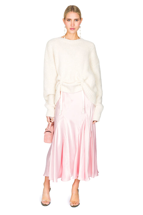 Side stance of white knit sweater with low hanging ties paired with a pink evening gown