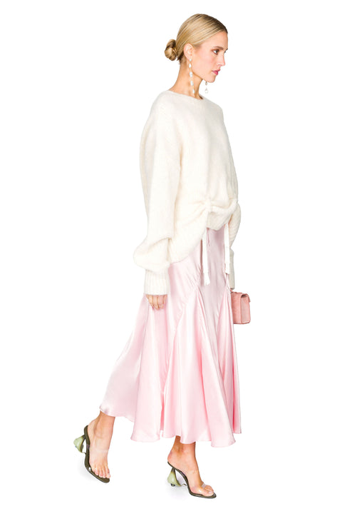 Side view of white knit sweater with low hanging ties paired with a pink evening gown
