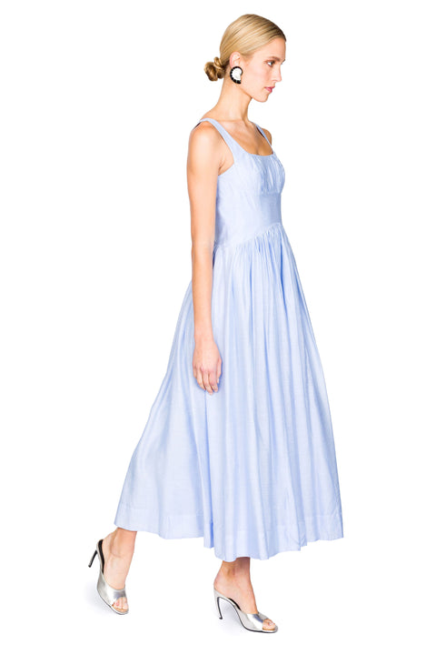 Woman stepping to the right wearing a light blue dress max on a white background