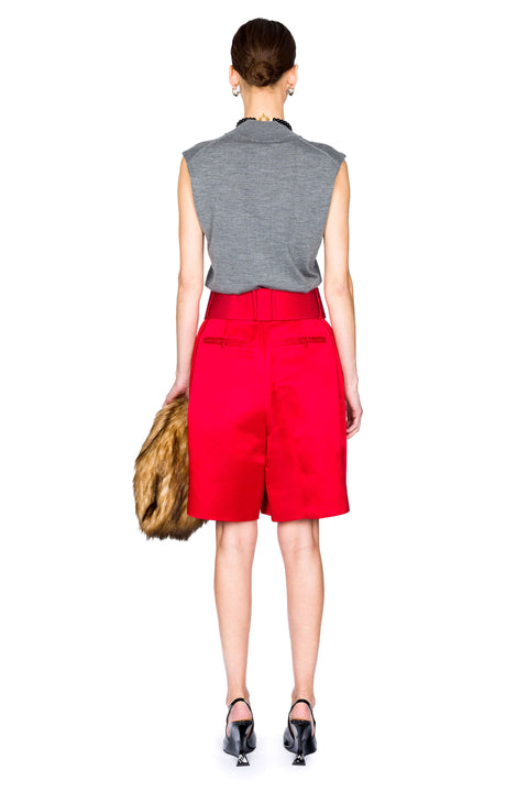 Woman facing away wearing a gray sleeveless top and red wide leg shorts and black heels on a white background