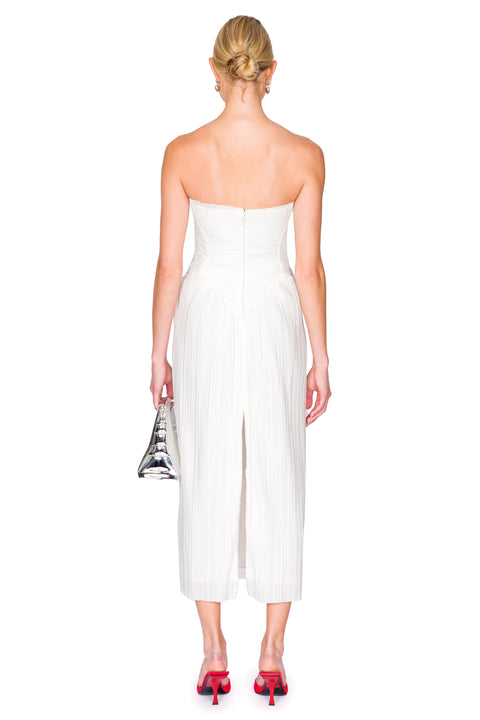Back view of a woman wearing a white strapless midi dress crafted from a plisse fabric which features a middle slit in the back and corset-style detailing. 