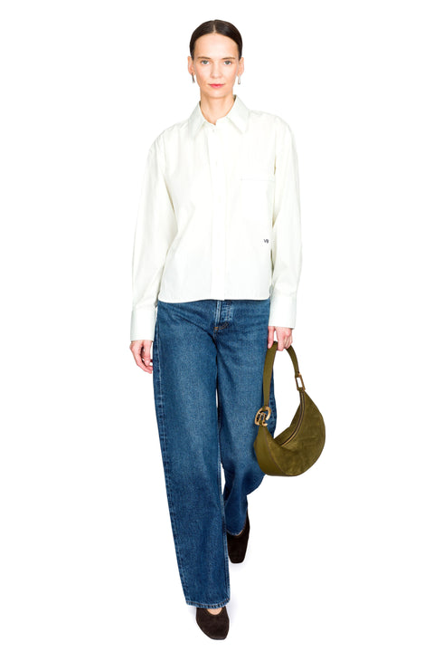 Woman walking wearing a green button down and blue jeans, holding a green handbag on a white background