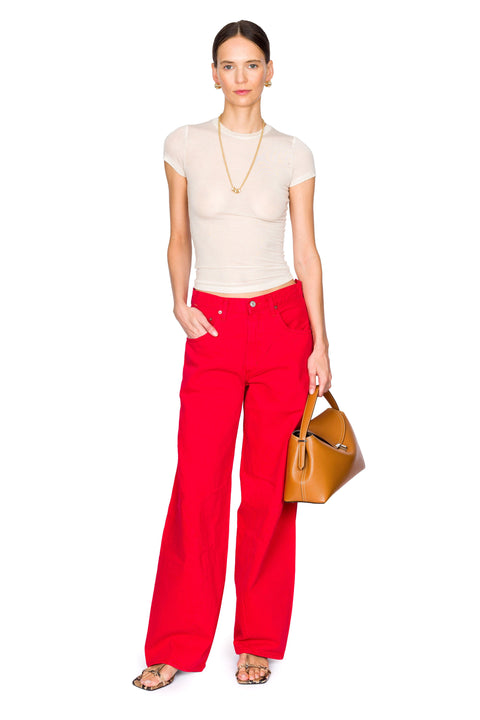 Woman wears sheer baby t-shirt with red denim and brown leather bag.