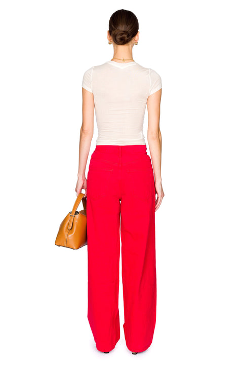 Back view of woman wearing red denim and sheer baby t-shirt hold a brown leather handbag.