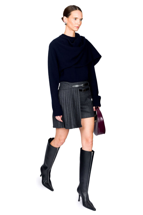 Woman walking wearing a navy sweater, gray pinstripe skirt, and black knee-high boots on a white background