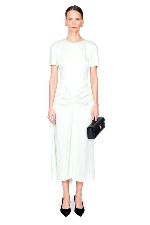 Woman wearing a light green satin dress holding a black clutch on a white background