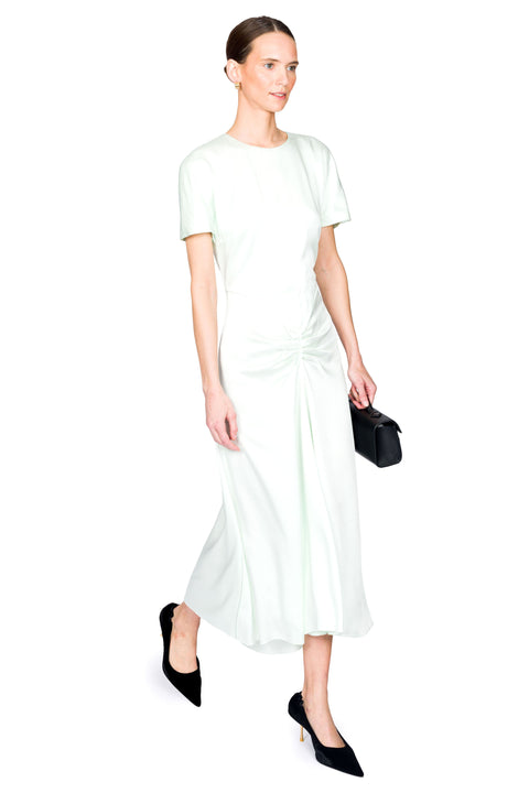 Woman talking a step wearing a light green midi dress holding a black clutch against a white background