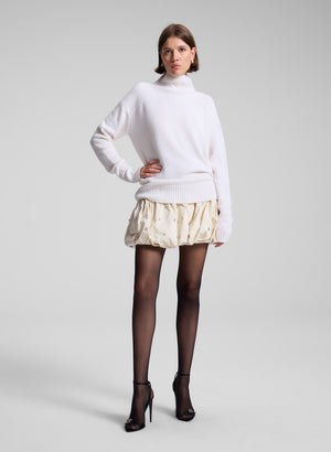 Women wears white sweater and cream embellished skirt.