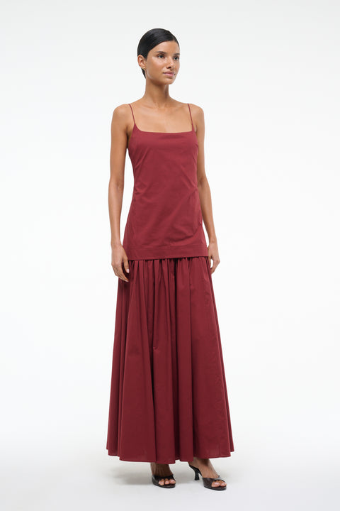 Woman wearing a deep red maxi dress that features a column bodice layered over a full skirt, paired with black kitten heels. 
