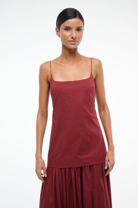 Close up of a woman wearing a deep red maxi dress that features a column bodice layered over a full skirt. 