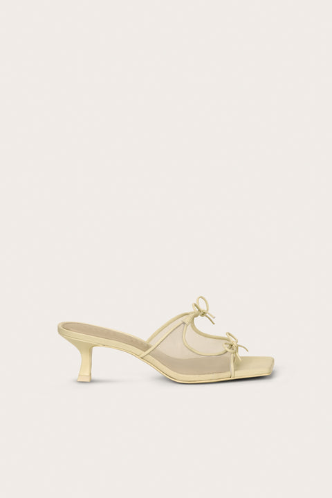 Side profile of a cream, open-toe kitten heal that features a mesh side panel design and two bows on the top of the foot. 