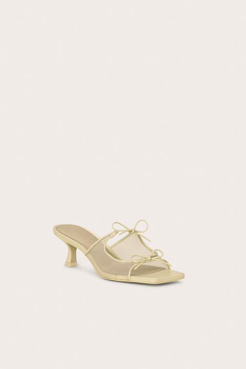Front profile of a cream, open-toe kitten heal that features a mesh side panel design and two bows on the top of the foot. 