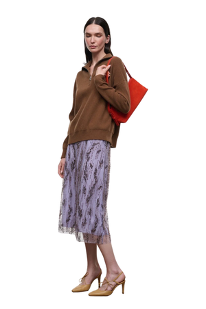 A woman modeling a brown half-zip pullover sweater, a light purple patterned midi skirt, and tan high-heeled pumps, carrying a bright red shoulder bag against a plain white background.