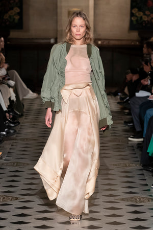 Model walking down a runway wearing the deconstructed pants with shirt detail in beige organdy.