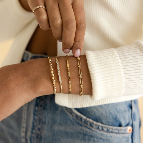 Woman's arm styled with different yellow gold bracelets.