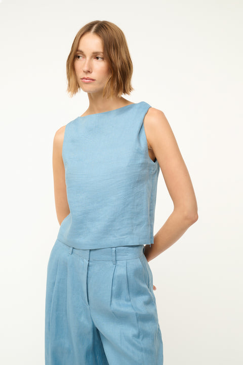 Close up of a woman wearing a blue linen tank top with a twist detail in one shoulder, paired with matching trousers. 