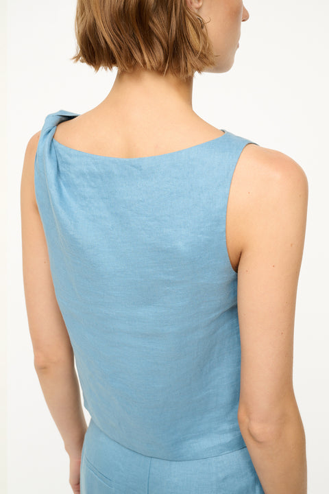 Close up back view of a woman wearing a box blue linen tank top hat features a twist detail on one shoulder. 