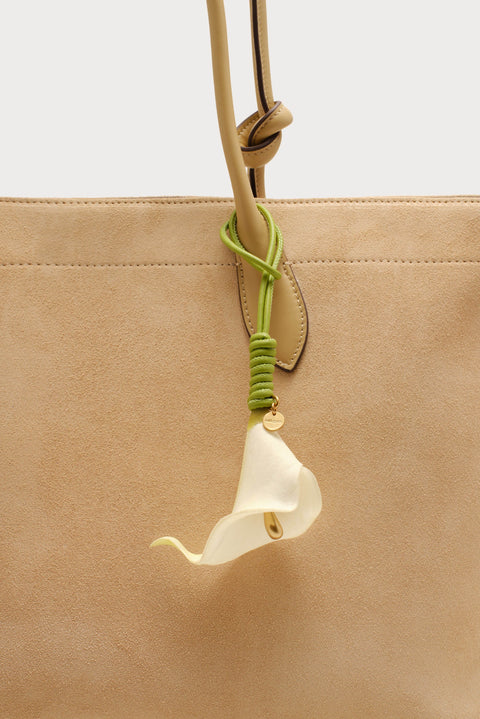Beige handbag with a white flower charm on a light gray background