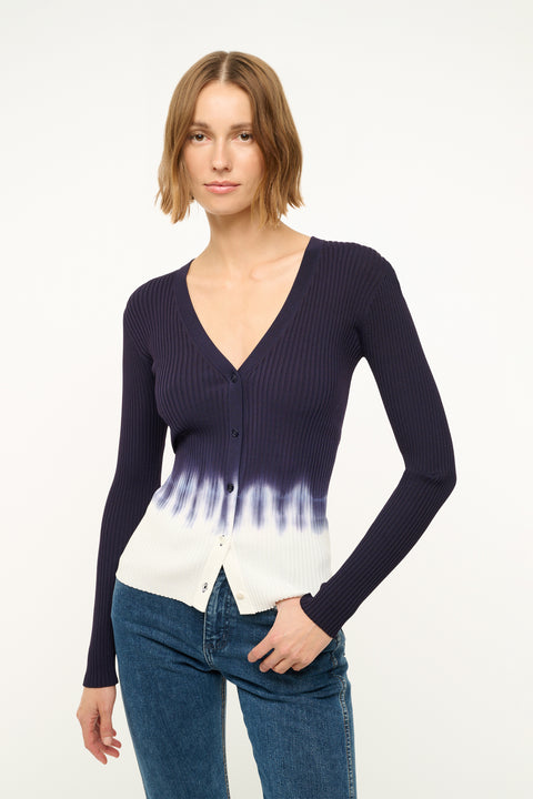 Close up of a woman wearing a fitted, rib-knit cardigan that features a deep-V and a navy to white tie dye effect, paired with jeans.