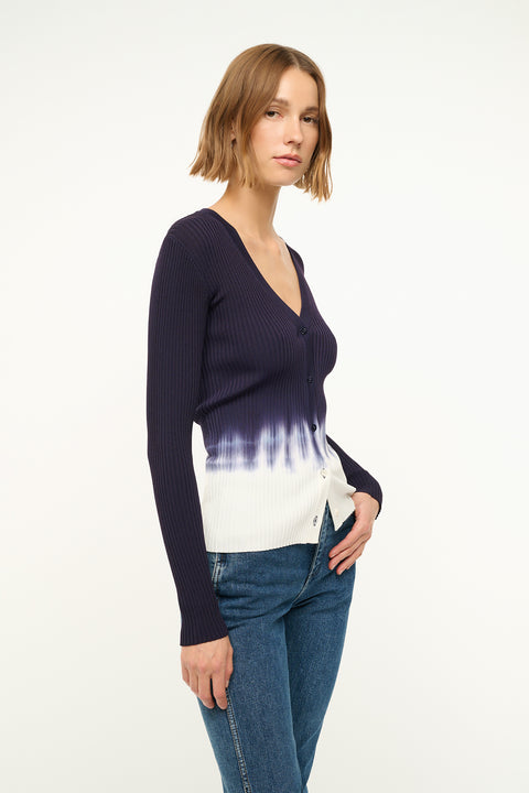Side view of a woman wearing a fitted, rib-knit cardigan that features a deep-V and a navy to white tie dye effect.  