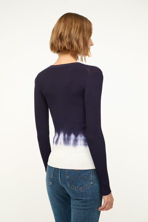 Back view of a woman wearing a fitted, rib-knit cardigan that features a deep-V and a navy to white tie dye effect.  