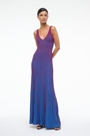 Woman wearing a blue knit maxi dress that features contrast red ribbing, a deep V, and a fitted silhouette.